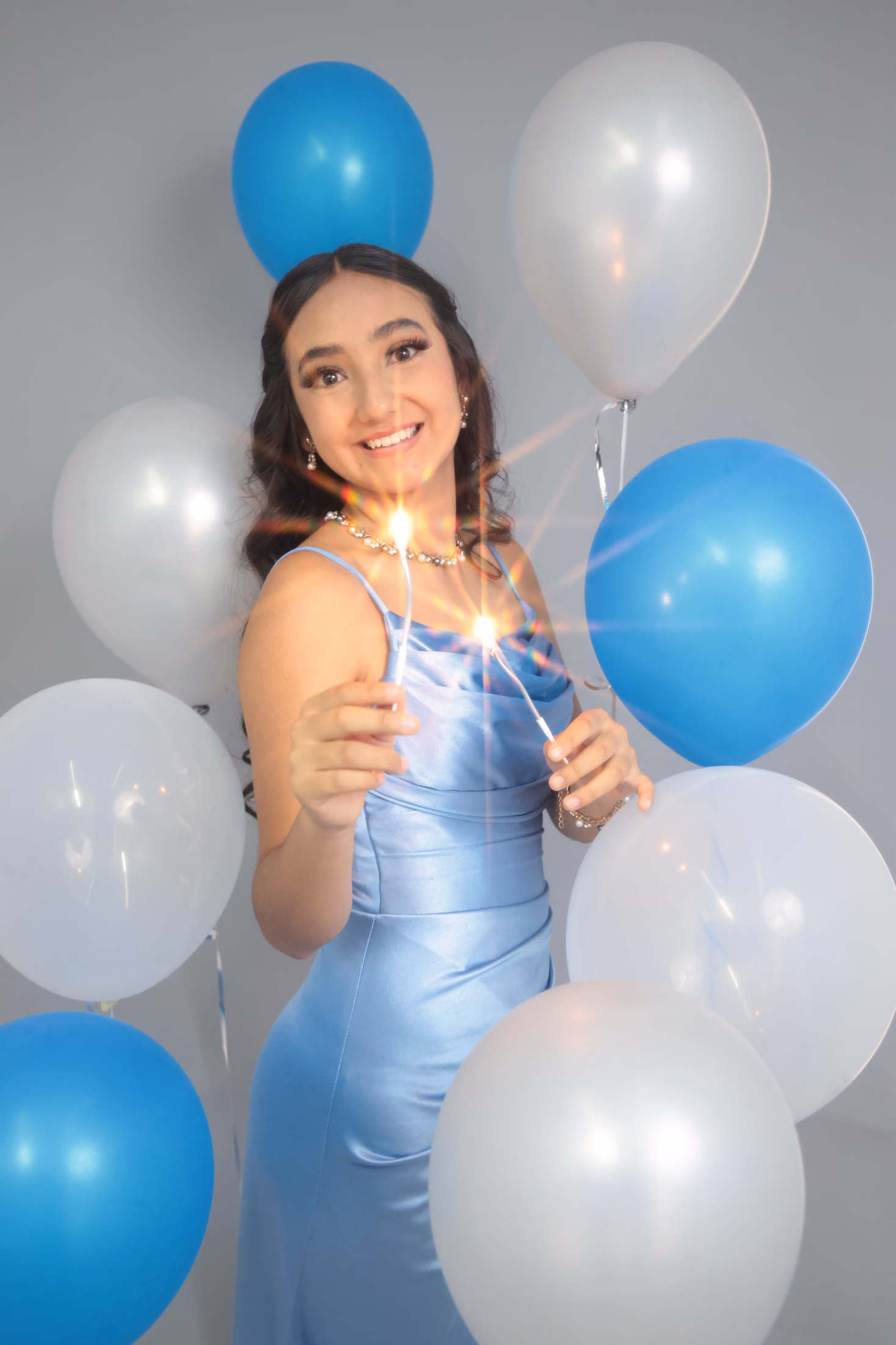 Quinceañera sosteniendo luces de bengala entre globos